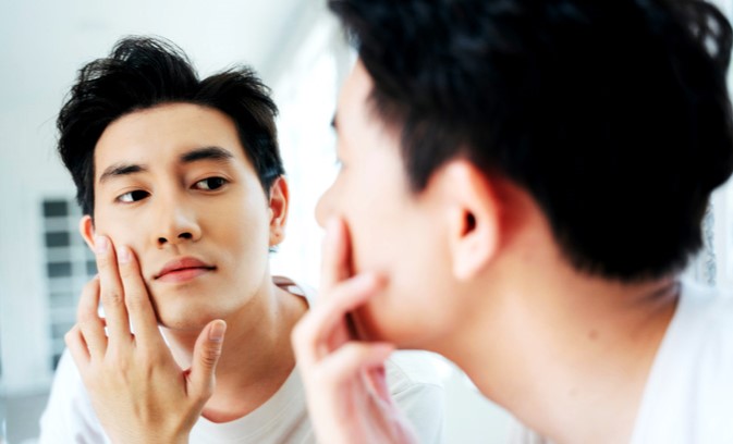 남성이 거울을 보면서 피부를 확인하고 있다